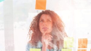 Vrouw Kijkt Naar Post Its Op Glazen Wand Ter Illustratie Van Nadenken Over AI Integreren In Werkproc.jpeg